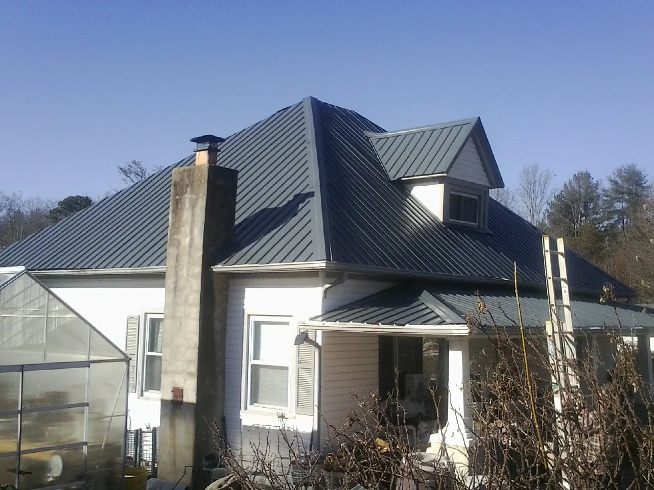Dark blue standing seam metal roof on a white farmhouse with dormer — Slate & Tile Roof Repair by Roofing Brothers in Burnett