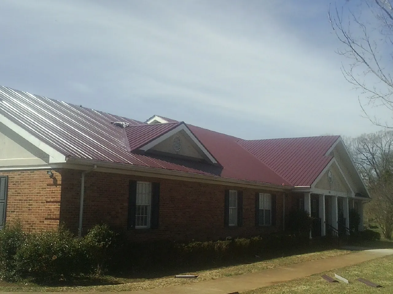 Red metal roof with gabled entries on a long brick building, from a Hail Damage Roof Repair job in Burnett