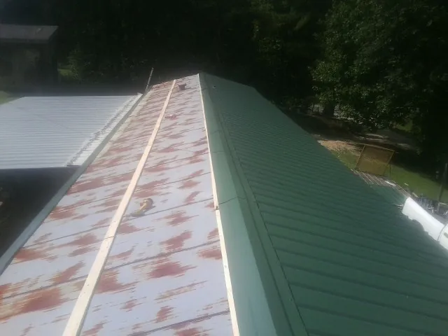 Old rusted panels beside newly installed green metal roofing — Wind Damage Roof Repair by Roofing Brothers in Burnett