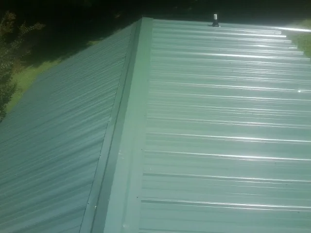 New green metal panels meeting at the ridge of a roof — Flat Roof Repair work by our crew in Burnett