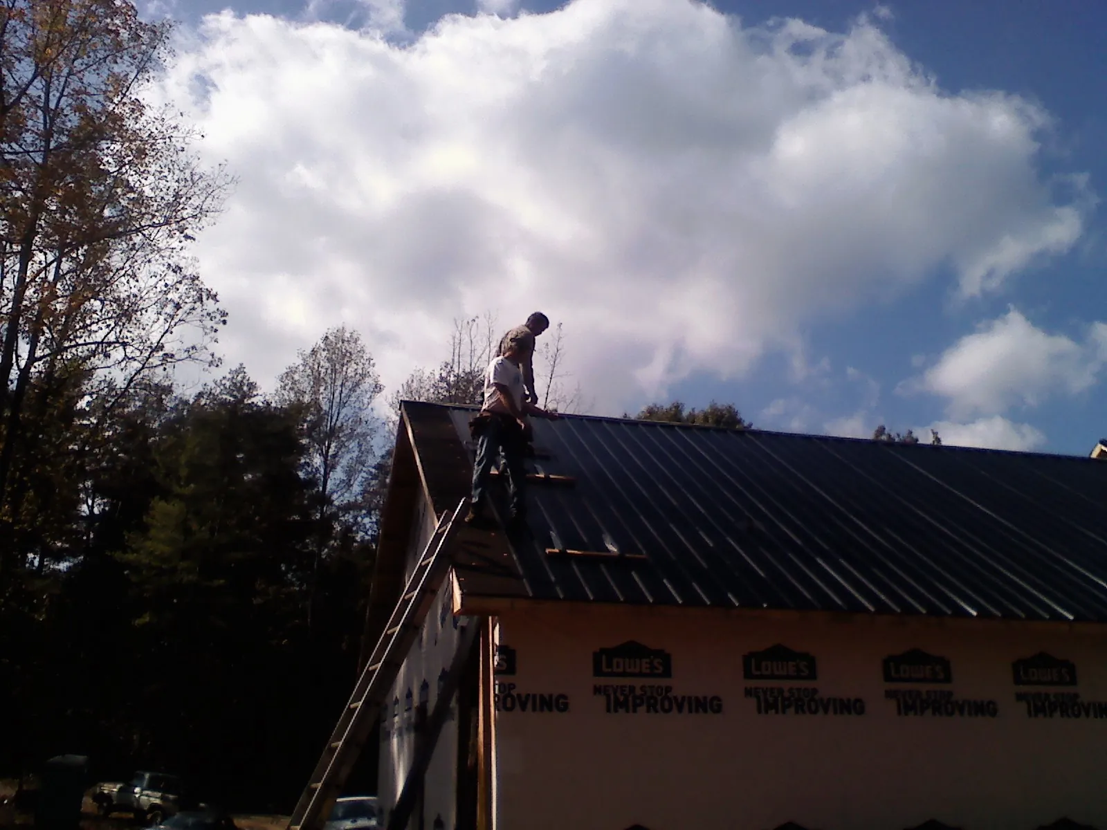 Roofer fastening dark metal panels high against a cloudy sky, from a Roof Inspection job in Burnett