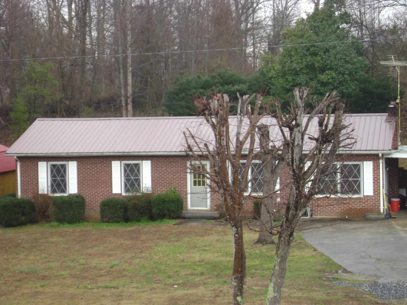Mauve metal roof on a brick ranch home behind bare trees in Burnett