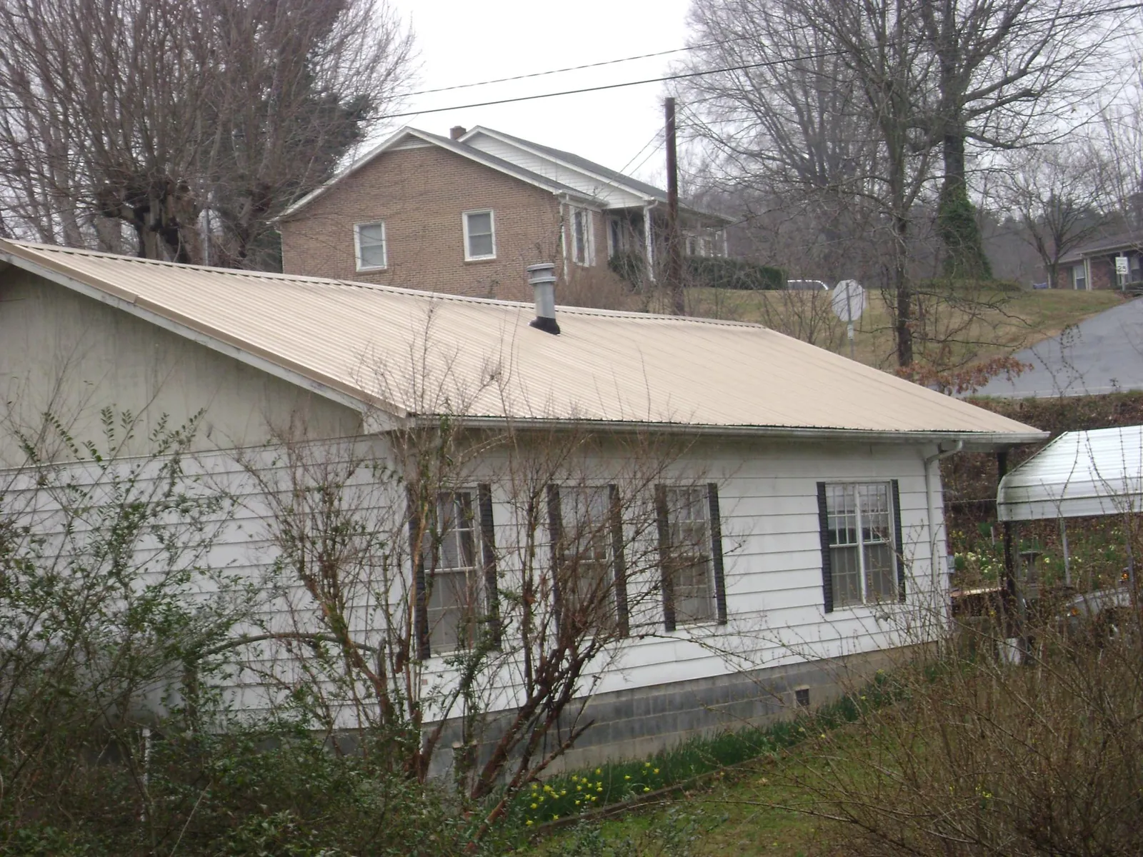 Tan metal roof on a white sided house set into a hillside — Commercial Roofing by Roofing Brothers in Burnett