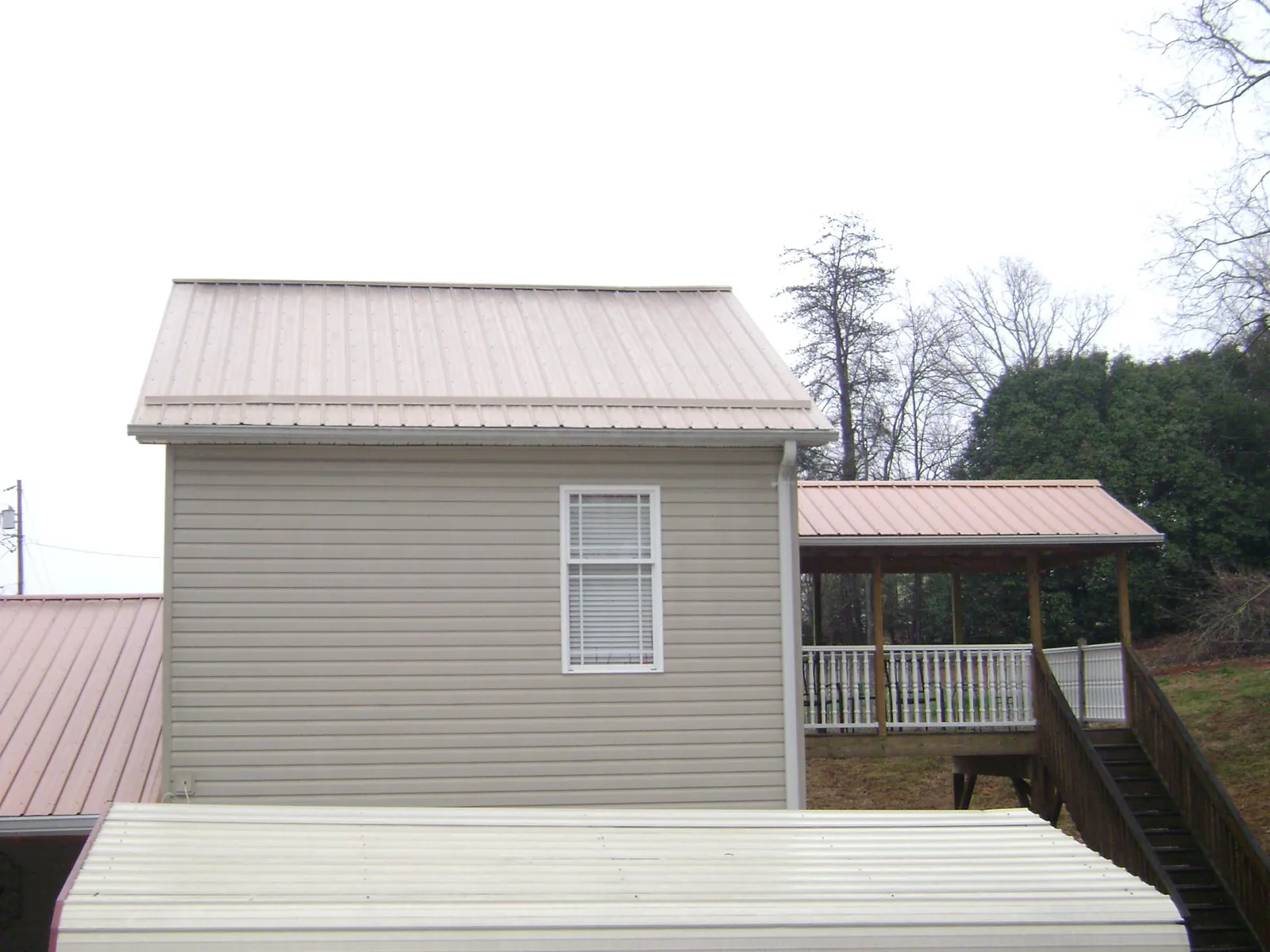 Tan metal roofs on a two story addition and attached porch, from a Roof Replacement job in Burnett