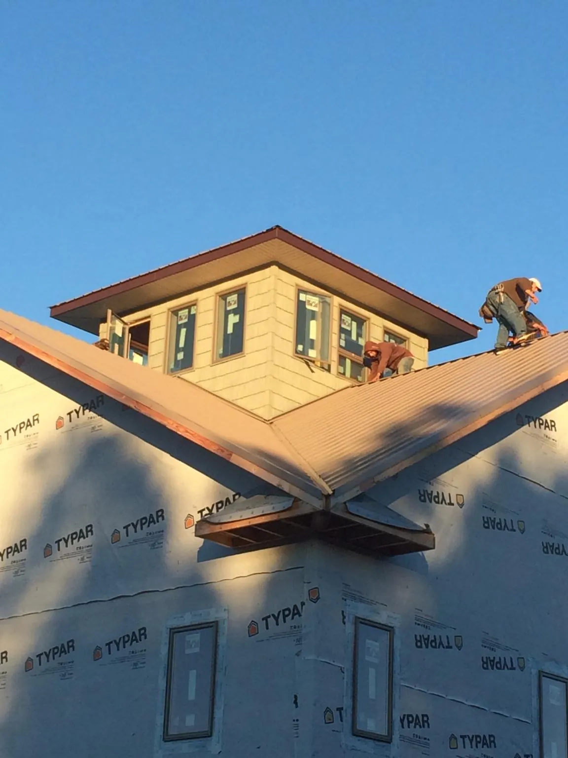 Roofers working around a rooftop cupola on a new metal roof at sunset — Roof Waterproofing in Burnett by Roofing Brothers